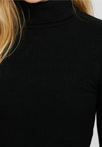 Pull en col roulé noir avec une texture côtelée, une coupe ajustée et un col haut, fabriqué dans un tissu doux et extensible.