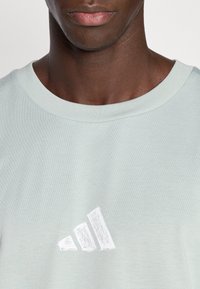 Ανοιχτό πράσινο κοντομάνικο μπλουζάκι από απαλό ύφασμα, με λευκό, ανάγλυφο λογότυπο Adidas στο στήθος. Στρογγυλή λαιμόκοψη.