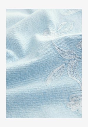 Gaiši zils džinsu audums ar mīkstu tekstūru, ar baltām izšūtām ziedu dizainiem. Virsma ir nedaudz krunkaina.