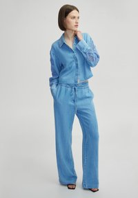 Camisa de mezclilla azul claro cortada con mangas de encaje intrincadas, combinada con pantalones de pierna ancha a juego, que presentan una cinturilla con cordón.