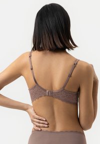 Rintaopas pitsi takaosalla hillityssä mauve-värissä, jossa on säädettävät olkaimet, hakas suljenta ja aallotettu pitsireuna. Silkkinen kangastuntuma.