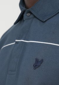 Μπλε κοντομάνικη μπλούζα πόλο από απαλό βαμβάκι, με λευκή οριζόντια ρίγα και κεντημένο λογότυπο στο στήθος. Κλασικός γιακάς.