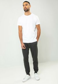 Weißes Kurzarm-T-Shirt kombiniert mit dunkelgrauen Sweatpants mit Kordelzug und neongrünen Akzenten, getragen mit weißen Sneakern.