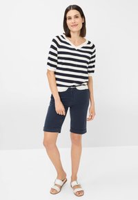 Marineblau-weiß gestreiftes Kurzarmshirt mit V-Ausschnitt, kombiniert mit marineblauen Shorts mit eingeschlagenem Saum und weißen Rutschsandalen.