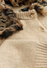 Pull beige avec une texture douce, doté d'un col en fausse fourrure à imprimé léopard, de deux boutons et de détails côtelés le long des bords.