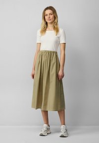 Lightweight, ribbed white t-shirt paired with a long, khaki green, elastic-waist skirt. Completed with gray and white athletic shoes.