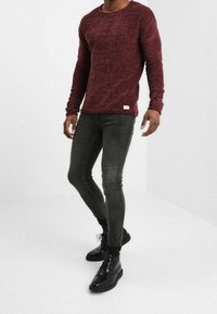 Bordowa teksturowana koszula z długim rękawem i okrągłym dekoltem, zestawiona z dopasowanymi ciemnoszarymi dżinsami i czarnymi butami na sznurowadła.