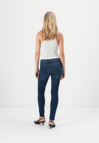 Sötétkék farmer skinny farmernadrág, magas derékkal, öt zsebbel és slim fit szabással. Világosszürke trikóval és fekete magassarkú cipővel viselve.