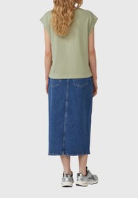 Groene top met korte mouwen, denim midi-rok en zilveren sneakers. De rok heeft achterzakken en een rechte pasvorm met een zoomlijn op halverwege het onderbeen.