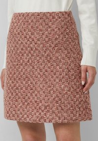 Een knie-lange roestvrijstalen rok in een textuur van roze en bruin tweed, gedragen met een witte trui met lange mouwen, weergegeven van taille tot halverwege de dij.