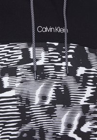 Top de Calvin Klein en blanco y negro con un diseño texturizado, doble cordón negro y un logo destacado en la banda.