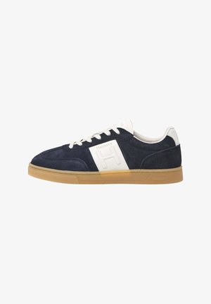 Baskets en daim bleu marine avec des accents blancs, arborant un logo "H" bien en évidence. Une semelle en caoutchouc et des lacets blancs complètent le design.