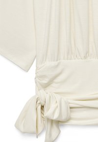 Top de tela color crema con mangas cortas, cintura fruncida y un gran detalle de nudo atado en el lado inferior.