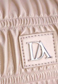 Cuero rosa pálido con textura recogida, que presenta un parche de logo rectangular embosado con "DA" en metal plateado.