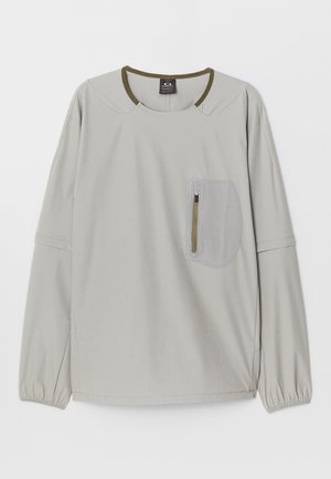 Light gray long-sleeve top with round neckline, elastic cuffs, and a textured patch pocket featuring a zipper on the front.