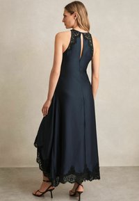 Vestito senza maniche di un blu scuro con orlo rifinito in pizzo e dettagli in pizzo sulle spalle. Presenta un'apertura a chiave sul retro e un design fluido.