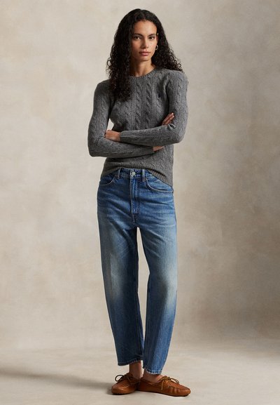 Szary sweter z grubym splotem, średniej wagi. Jasnoniebieskie proste dżinsy z wyblakłymi akcentami. Brązowe buty w stylu mokasynów. Prosty design.