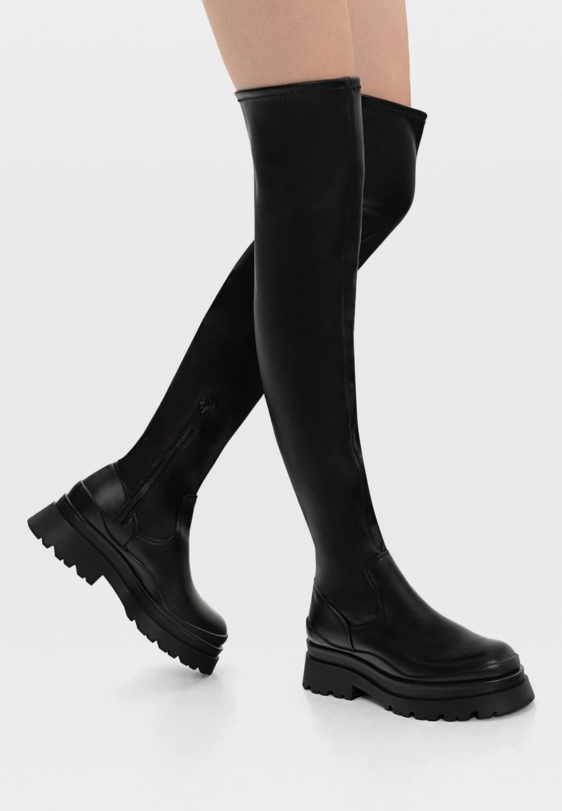 Bottes noires au-dessus du genou en cuir lisse, avec une semelle épaisse, une fermeture éclair sur le côté et un design élégant et ajusté.