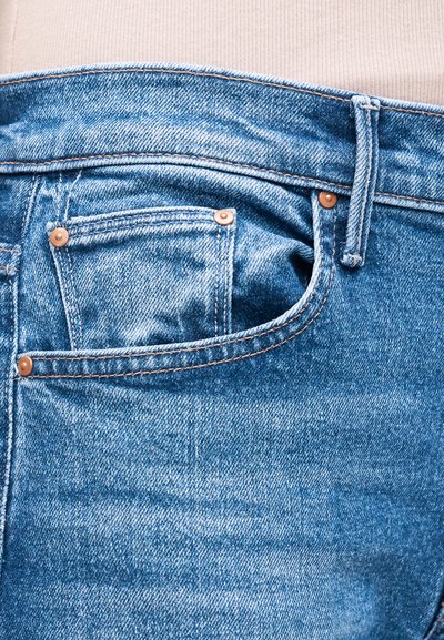 Κοντινή λήψη μέσης τζιν παντελονιού σε ανοιχτό μπλε χρώμα με ορατό λουράκι ζώνης, μπροστινή τσέπη και μικρή τσέπη για κέρματα, φορεμένο με μπεζ ριμπ λεπτομέρεια τοπ.