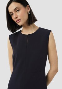 Robe sans manches bleu marine avec un col rond, un détail de fente sur le devant et une coupe ajustée avec des coutures minimales et des poches latérales.