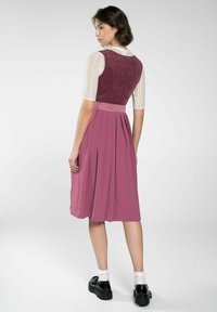 Kleid in knielanger Länge mit einem figurbetonten burgunderfarbenen Oberteil und einem plissierten rosa Rock; hat durchsichtige Spitzensäume und einen Taillenbund aus Satin. Schwarze Schuhe runden den Look ab.