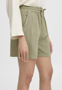 Grüne Baumwollshorts mit elastischem Bund und verstellbarem Kordelzug. Mit seitlichen Taschen und einer weichen, strukturierten Oberfläche.