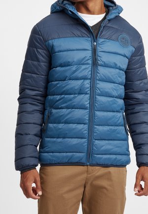 Giacca a vento blu con motivo trapuntato orizzontale, chiusura con zip, cappuccio e due tasche laterali. Presenta un logo rotondo sul petto.