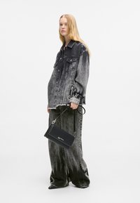 Grey acid-wash denim jacket and baggy jeans, paired with a small black handbag. Long, straight hair. Black shoes accent the outfit.