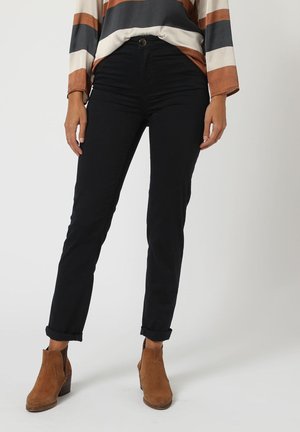 Pantalones slim-fit negros con una textura suave y puños enrollados, combinados con botas de tobillo marrones con detalles de costura y un tacón bajo.