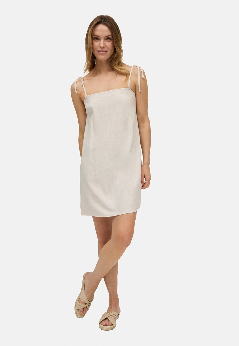 Vestido de verano de lino color beige claro con tirantes ajustables en los hombros, corte recto y textura mínima. Presenta un diseño de longitud hasta el muslo.