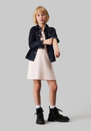 Giacca di denim, vestito rosa leggero e stivali militari neri con lacci. Calze e maniche della giacca arrotolate aggiungono dettaglio all'outfit.