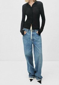 Černá dlouhá košile s knoflíky a slim fit, v kombinaci s volnými světle modrými džíny a špičatými černými lodičkami s bílými akcenty.