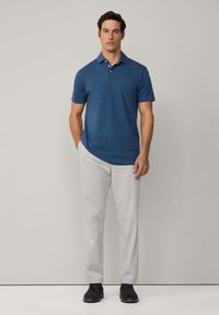 Kortärmad blå polo med krage, i kombination med ljusgrå byxor och marinblå skor. Enkel design, jämn textur och avslappnad passform.