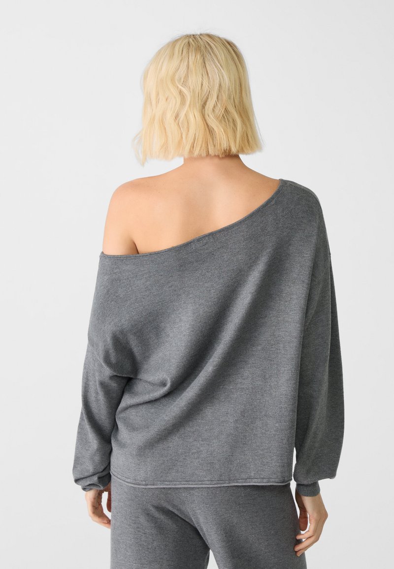 Szary sweter bez ramiączek z miękkiego materiału. Luźny krój z długimi rękawami i ściągaczami przy mankietach. Gładka tekstura z minimalnymi detalami szycia.