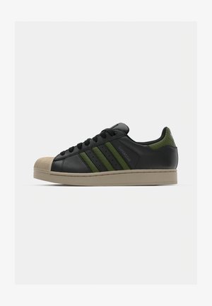 Schwarze Leder-Sneaker mit drei grünen Streifen, Gummikappe und beiger Sohle. Verfügt über auffällige Markenbezeichnung an der Seite.