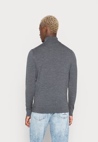 Grå langærmet strikket pullover med høj krave, ribbet tekstur og tætsiddende design, parret med lyseblå denim jeans.