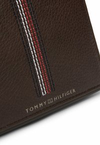 Brązowy skórzany portfel z trzema pionowymi haftowanymi paskami w kolorach czerwonym, białym i niebieskim, z srebrnym logo "TOMMY HILFIGER".