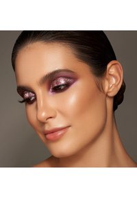 Primo piano di un volto con ombretto glitterato viola, pelle liscia e labbra morbide. I capelli sono raccolti, mettendo in risalto l'orecchio e la mandibola.