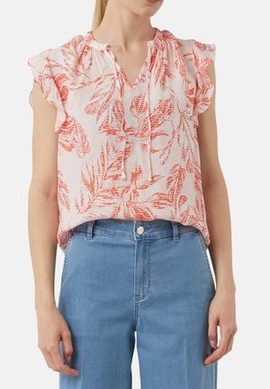Kurzarmbluse mit einem pinken und orangefarbenen Blattmuster, Rüschensleeves und einem V-Ausschnitt, kombiniert mit hellblauen hochgeschnittenen Jeans.