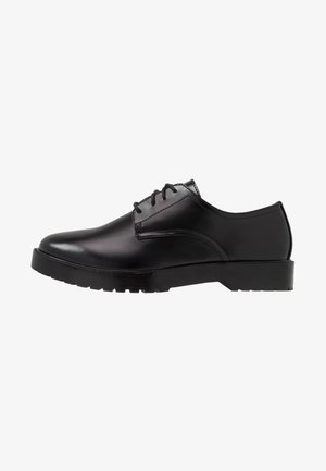 Chaussures en cuir noir avec un bout arrondi, une semelle plate et une finition lisse. Elles présentent un laçage traditionnel et des détails de couture subtils.