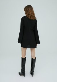 Robe mini noire avec de longues manches évasées, texture lisse et coupe droite. Associée à des bottes noires brillantes jusqu'au genou avec un motif reptile.