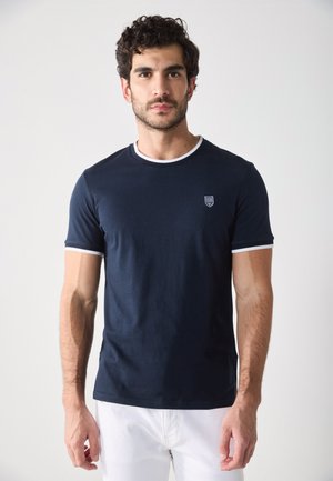 Camiseta de algodón azul marino con cuello y ribetes de las mangas en blanco, que presenta un pequeño emblema en el pecho. Mangas cortas, diseño de cuello redondo.