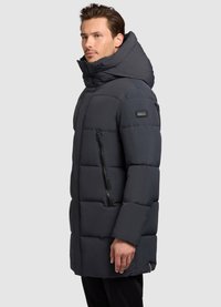 Padded temno siva jakna z visokim ovratnikom, stranskimi zadrgami in logotipno nalepko. Ima prešito zasnovo za izolacijo in toploto.