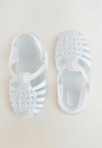 Genomskinliga plastsandaler med ett vävt mönster, med justerbara remmar och en slät yta, presenterade i en vy ovanifrån.