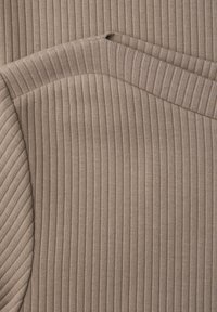 Zbliżenie na beżową dzianinę prążkowaną z złożonymi krawędziami, ukazującą pionowe i ukośne wzory prążków.