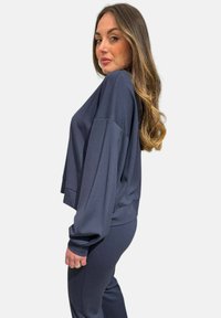 Maglia lunga a maniche lunghe di colore blu navy, oversize con spalle scese e orlo a costine; abbinata a pantaloni coordinati, con texture del tessuto liscia.