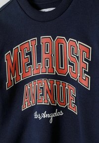 Felpa blu navy con la scritta "MELROSE AVENUE" in rosso e bianco. Presenta un collo a coste e una texture morbida. Design casual, adatta per l'uso quotidiano.