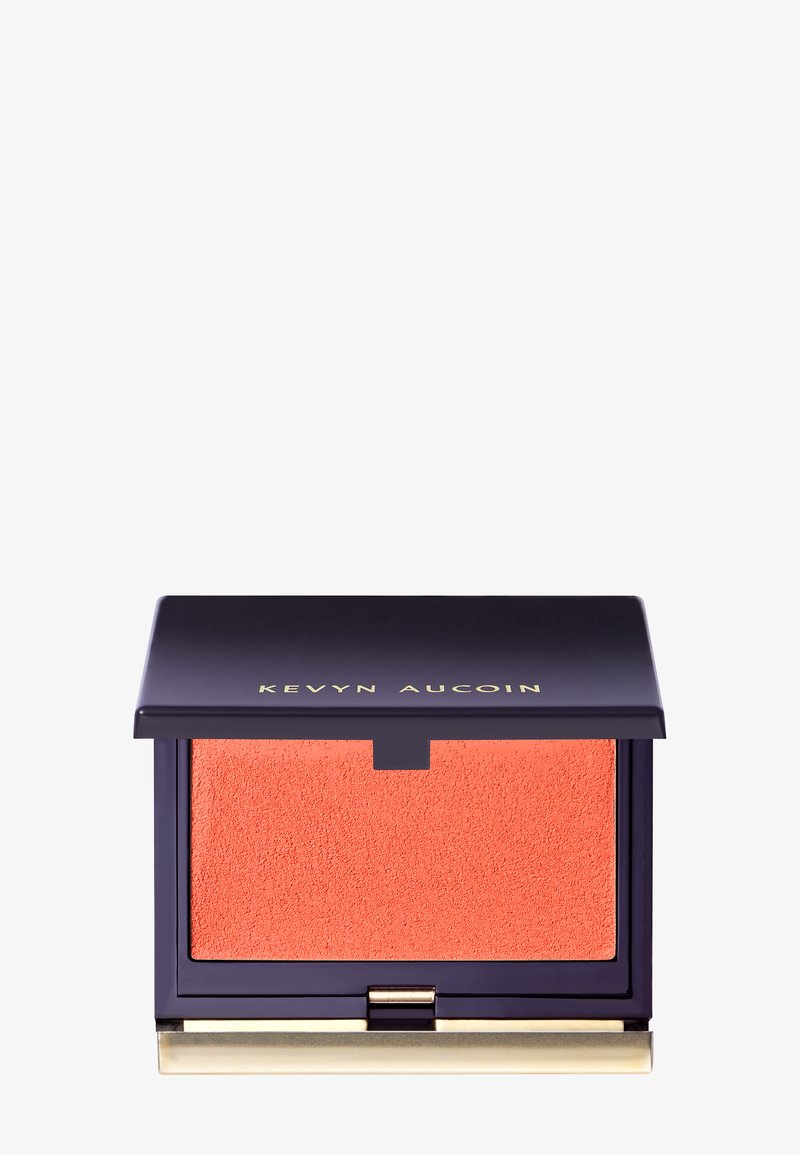 Blush arancione in una confezione quadrata con un coperchio blu navy e dettagli dorati. Superficie testurizzata e cerniera per un'apertura facile. Nome del marchio visibile.
