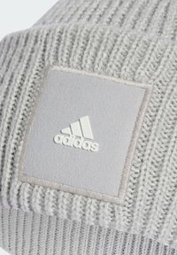 Berretto in maglia grigio con texture a costine, dotato di una toppa rettangolare grigia e del logo Adidas bianco. Tessuto morbido e design aderente.