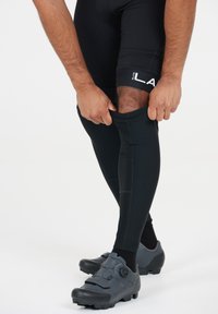 Svarta cykling benärmar med en åtsittande passform, med en slät yta och förstärkta sömmar, matchade med grå cykelskor.